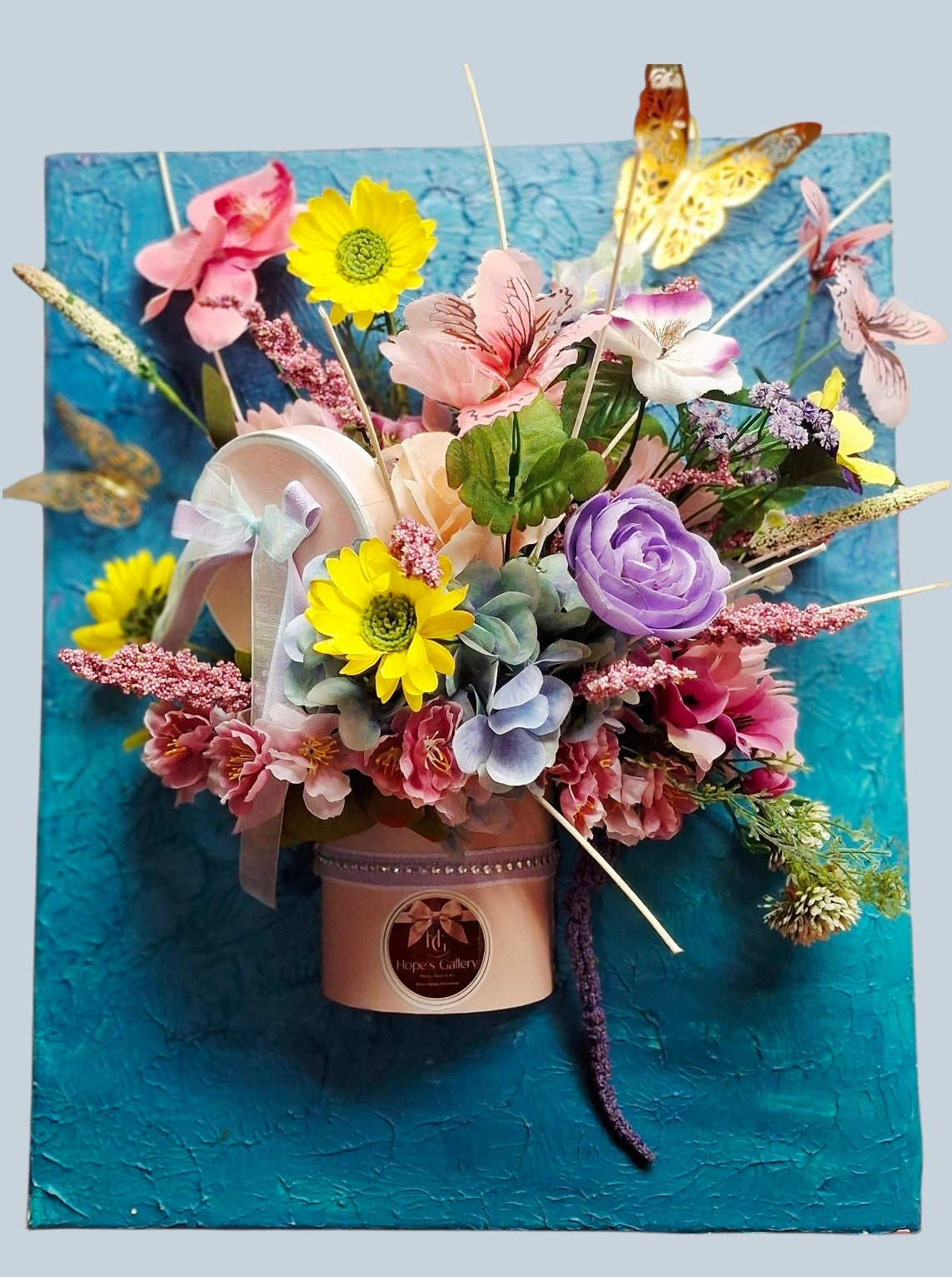Centro de mesa con flores mixtas coloridas y mariposas doradas en caja cilíndrica Hope's Gallery