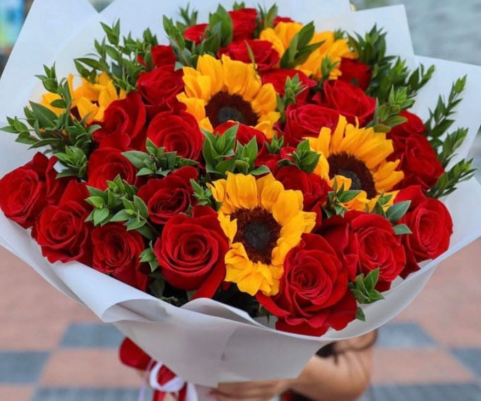 Ramo de rosas rojas con girasoles frescos envuelto en papel blanco