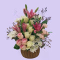 Arreglo floral en canasta de mimbre con lirios rosados, rosas blancas y rosadas, crisantemos y statice lavanda