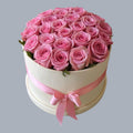 Caja redonda crema con rosas rosadas frescas y listón rosa en moño