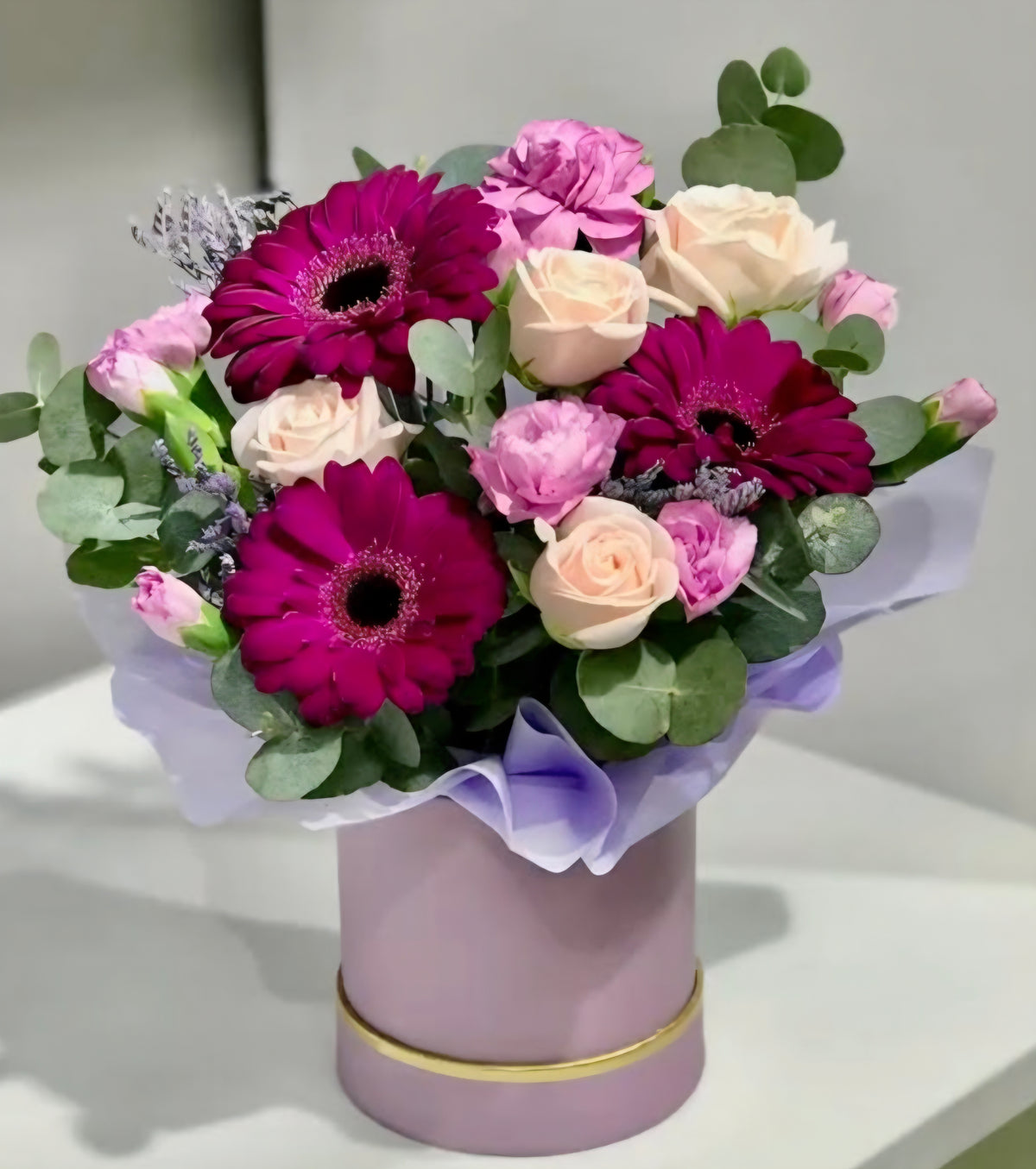 Mini caja lila con gerberas fucsia, rosas champán y claveles lila