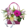 Arreglo de gerbera fucsia, mini rosas y alstroemerias en una caja tipo bolso rosa con lazo blanco