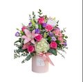 Arreglo de lirios rosados, rosas fucsia, hortensia blanca y lisianthus lila en caja redonda rosa con tarjeta